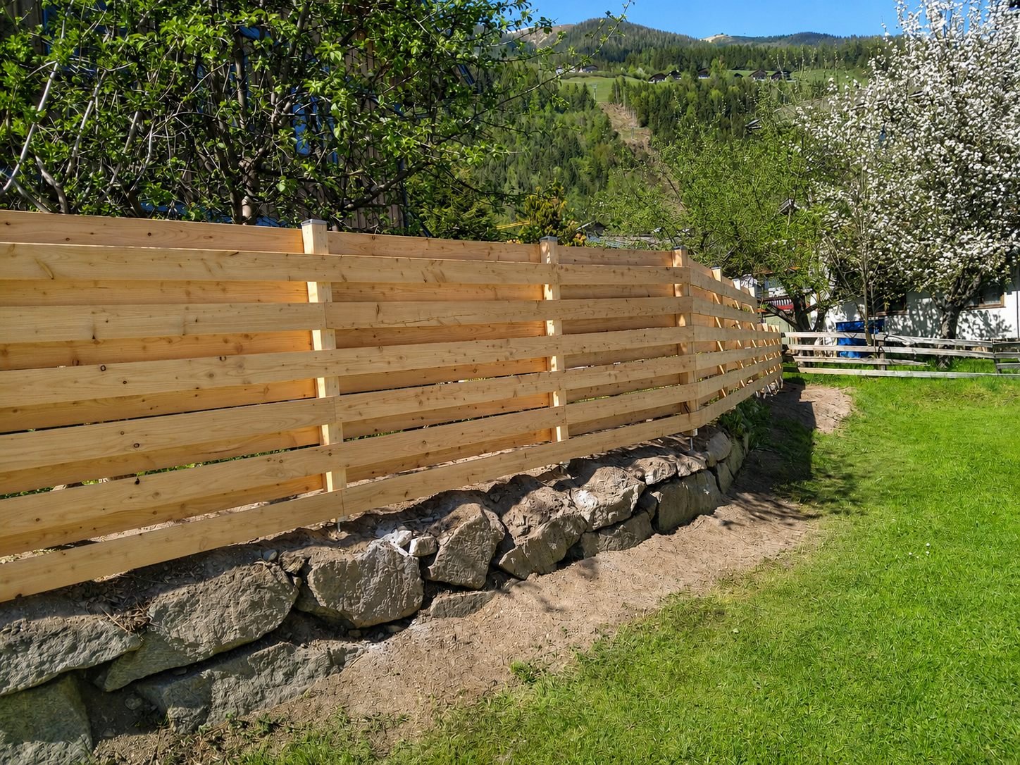 Neuer Holzzaun auf einer Natursteinmauer im Frühling