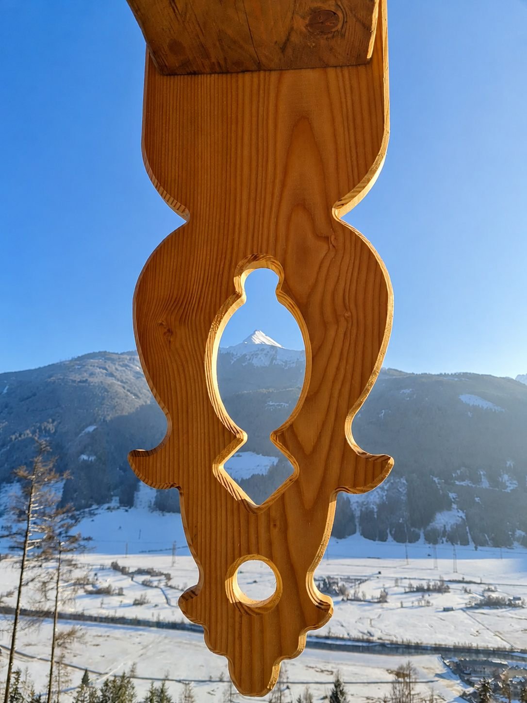Geschnitzter Balkonträger mit Blick auf einen verschneiten Berggipfel